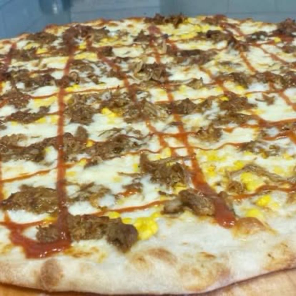 A Pizza Village V pizza topped with pulled pork, corn, mozzarella, and BBQ sauce drizzle.